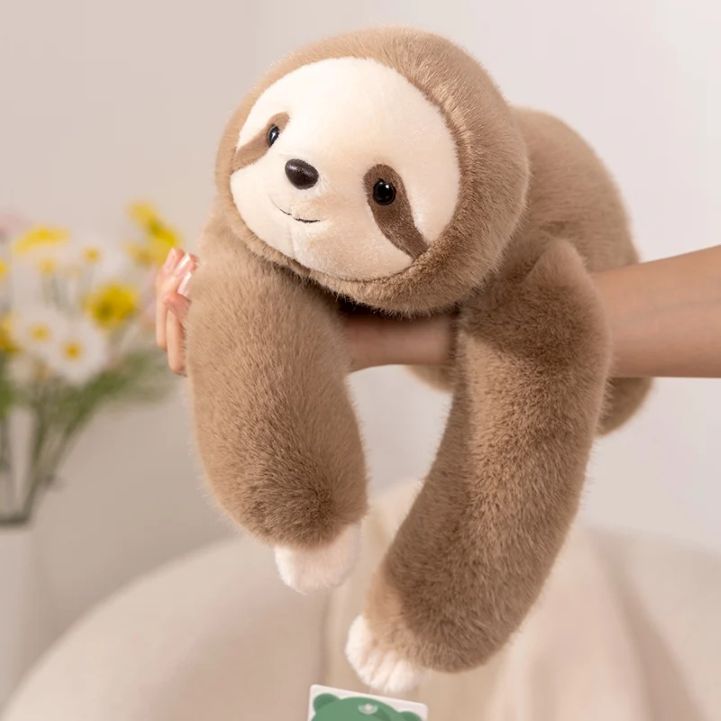 Plush sloth toy held by a hand with a blurred background
